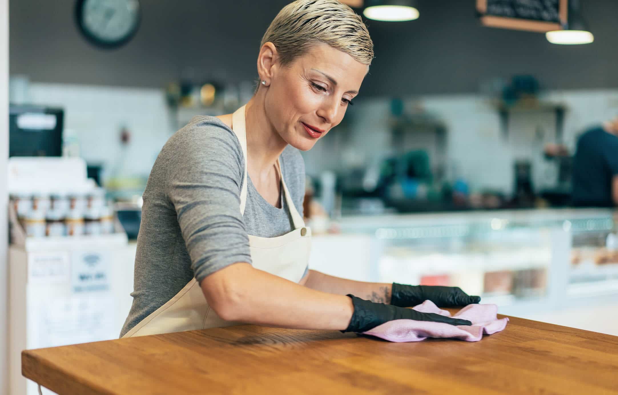 Woman cleaning with spray disinfectant and gloves in cafe