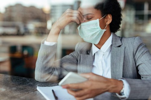 Exhausted African American businesswoman wearing protective face mask