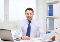 Smiling business man using a computer and holding documents