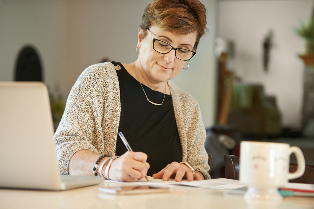 Mature woman making notes while working at home
