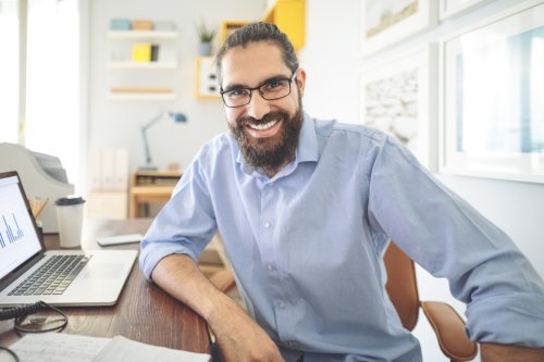 Man in a blue shirt smiles at desk