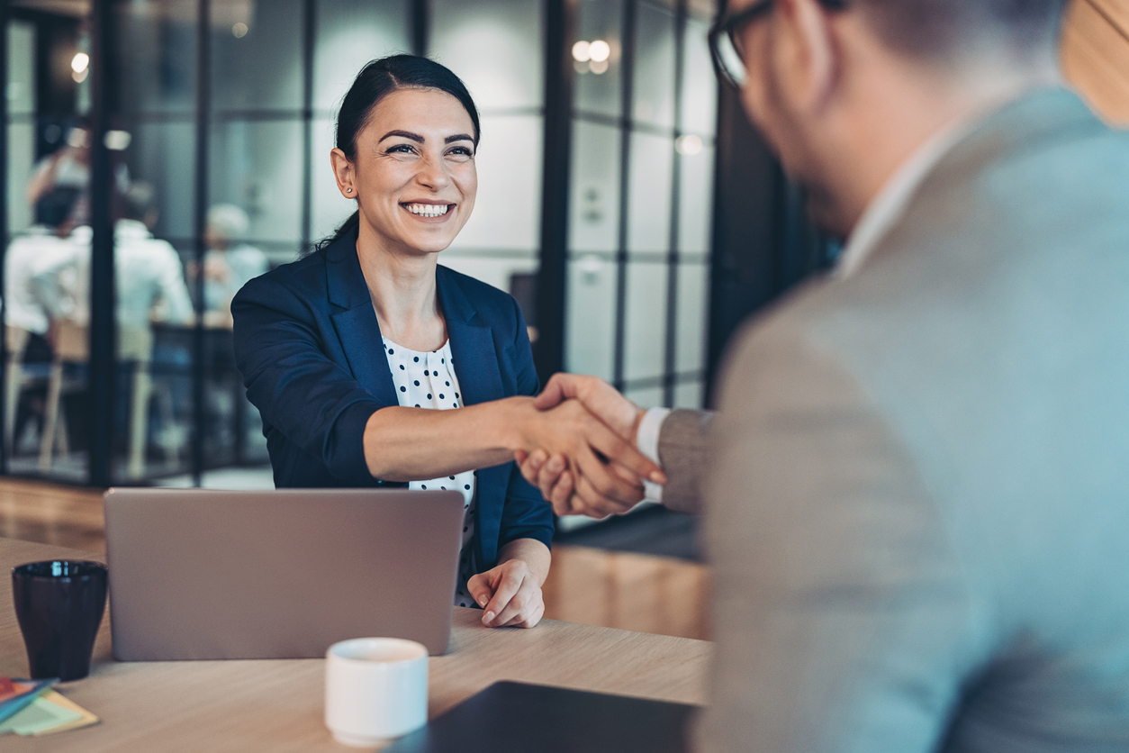 Business woman in professional attire shakes hand with male business man