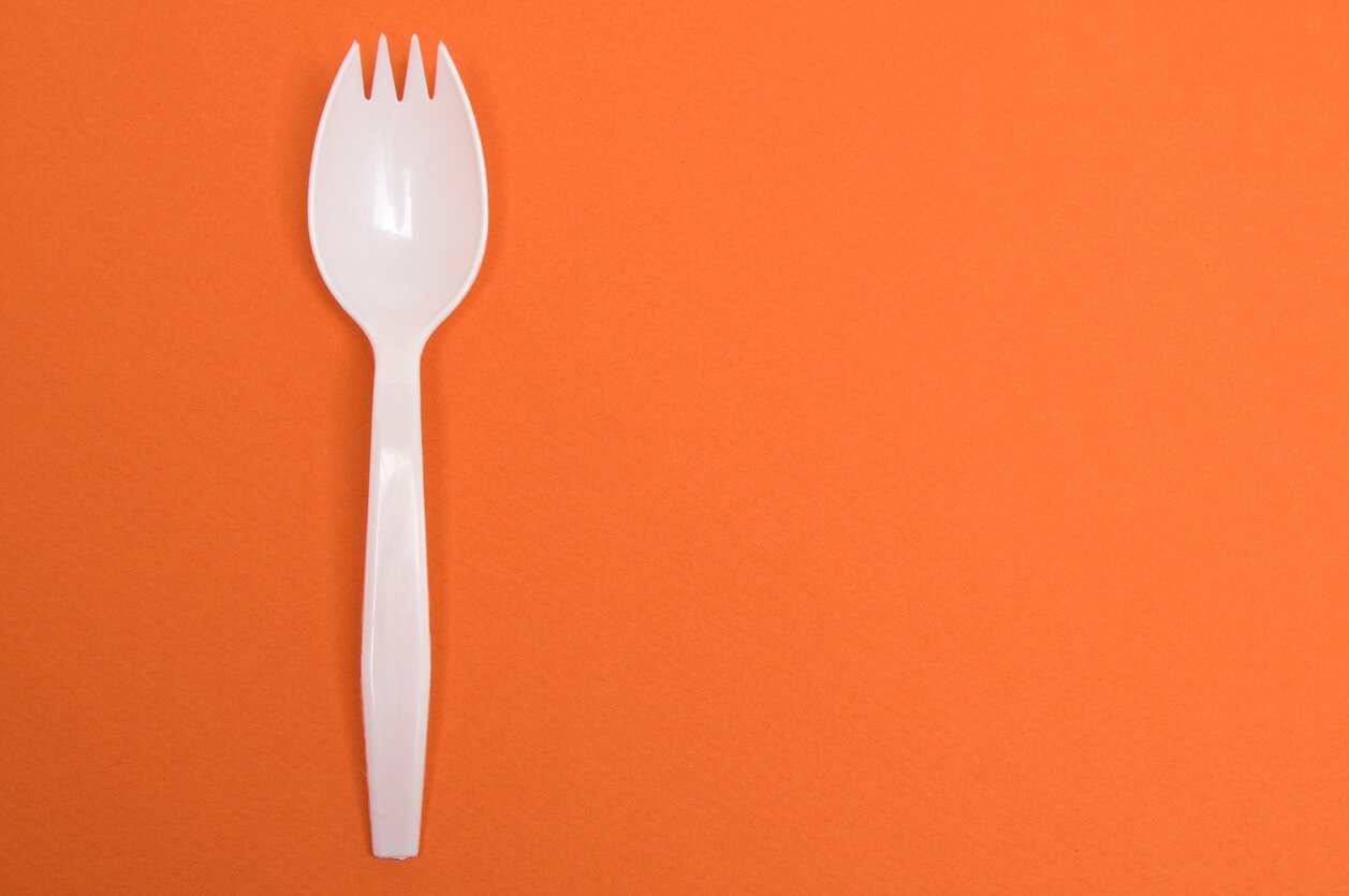 White plastic spork against an orange background