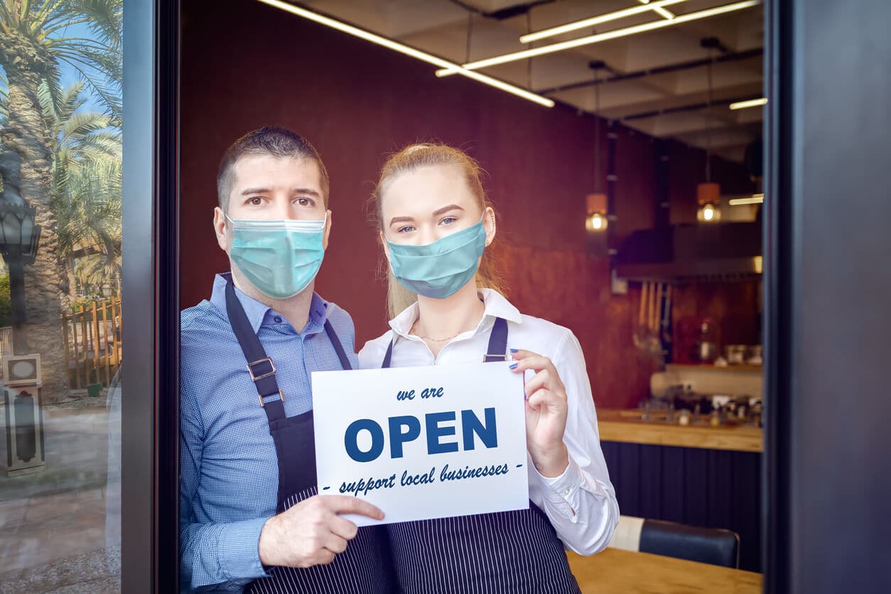 Two small business owners hold Open sign in front of their restaurant