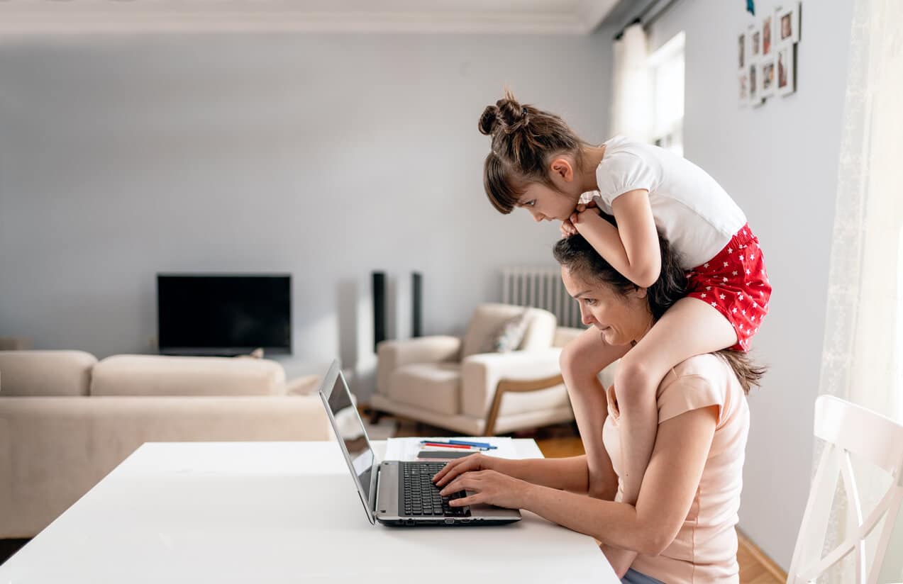 Woman working on her laptop with daughter on her shoulder