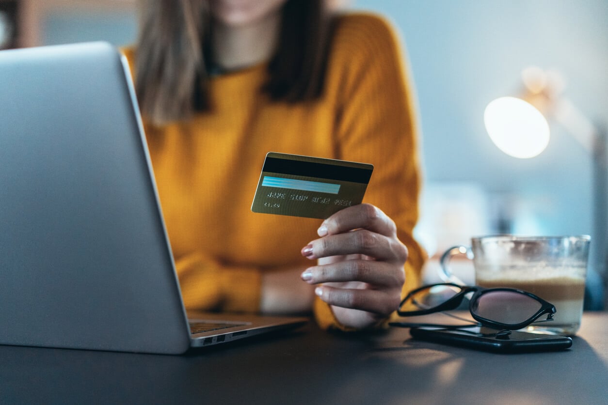 Woman working on laptop holds credit card in other hand