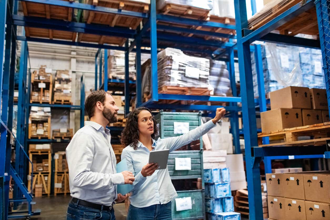 A male and a female employee checking inventory is a warehouse full of boxes.