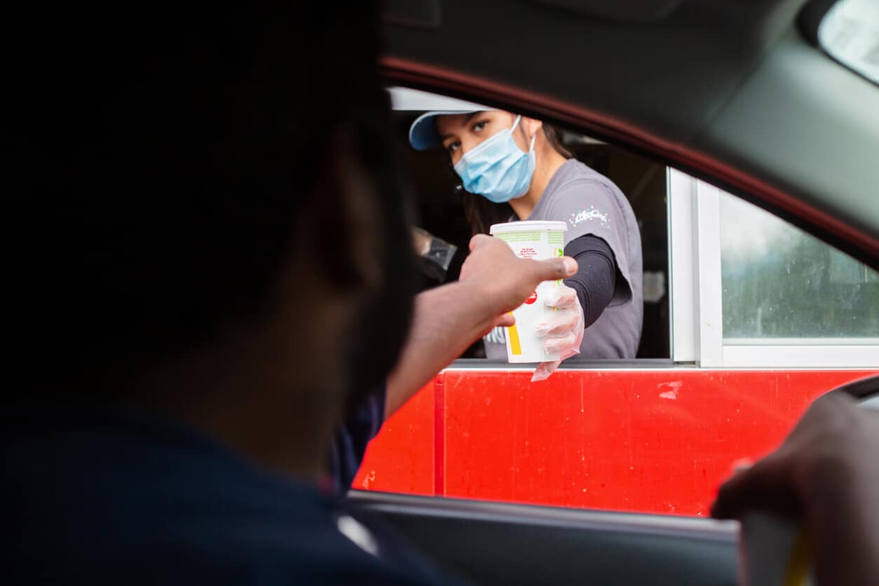 Fast food worker hands a drink to a customer in the drive thru